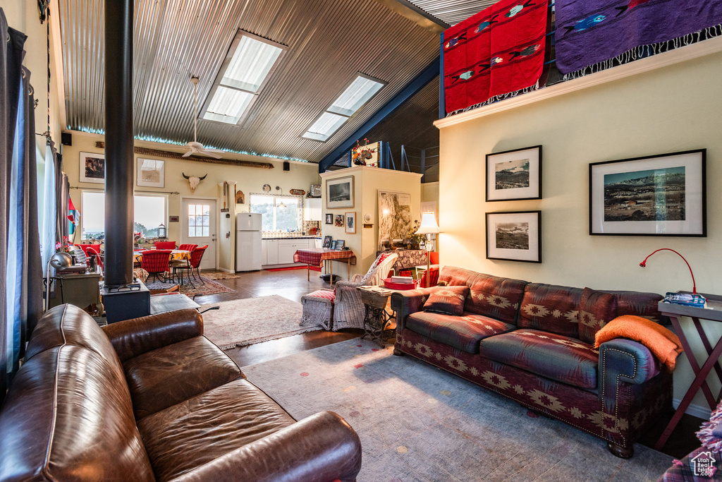 Living room with high vaulted ceiling, a skylight, hardwood / wood-style floors, and a wood stove