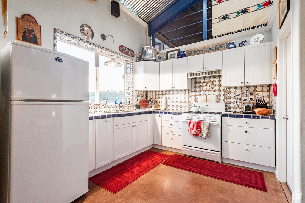 Kitchen with white cabinets, decorative backsplash, white appliances, and tile countertops