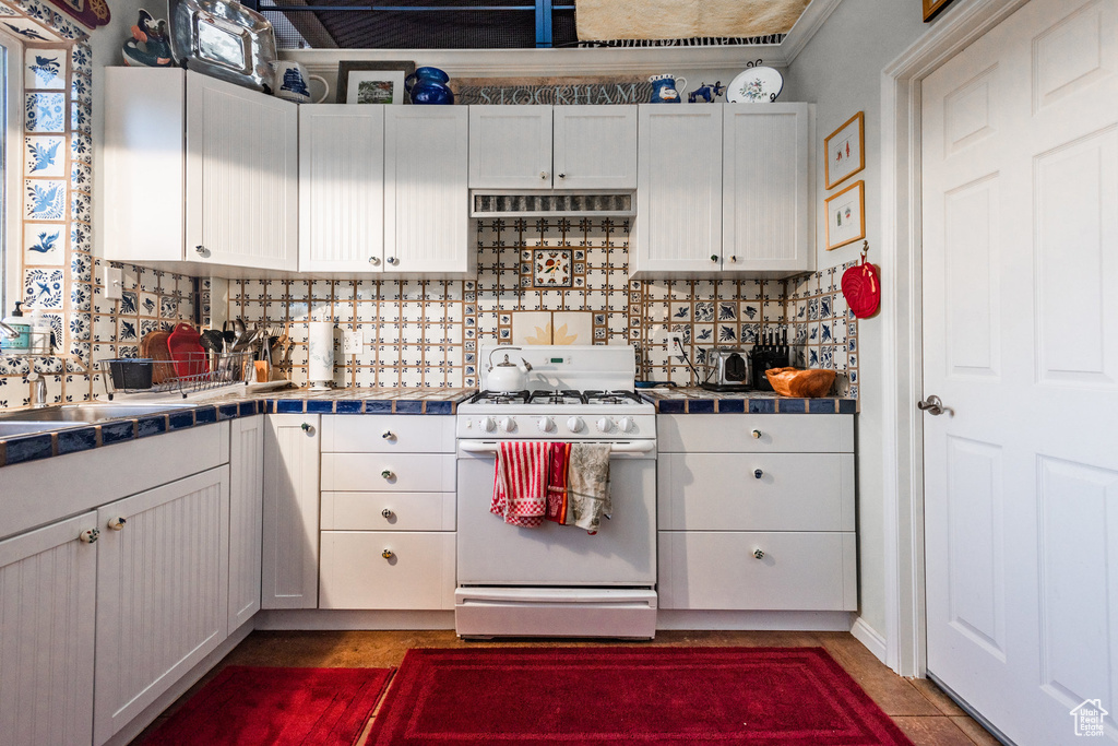 Kitchen with tile countertops, white cabinets, white range with gas stovetop, and backsplash