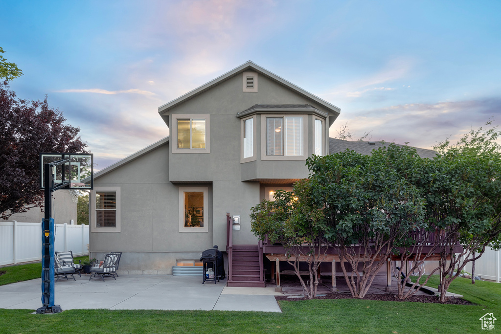 Back house at dusk featuring a deck, a patio, and a yard