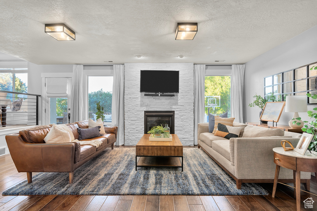 Living room featuring a stone fireplace, wood-type flooring, and a textured ceiling