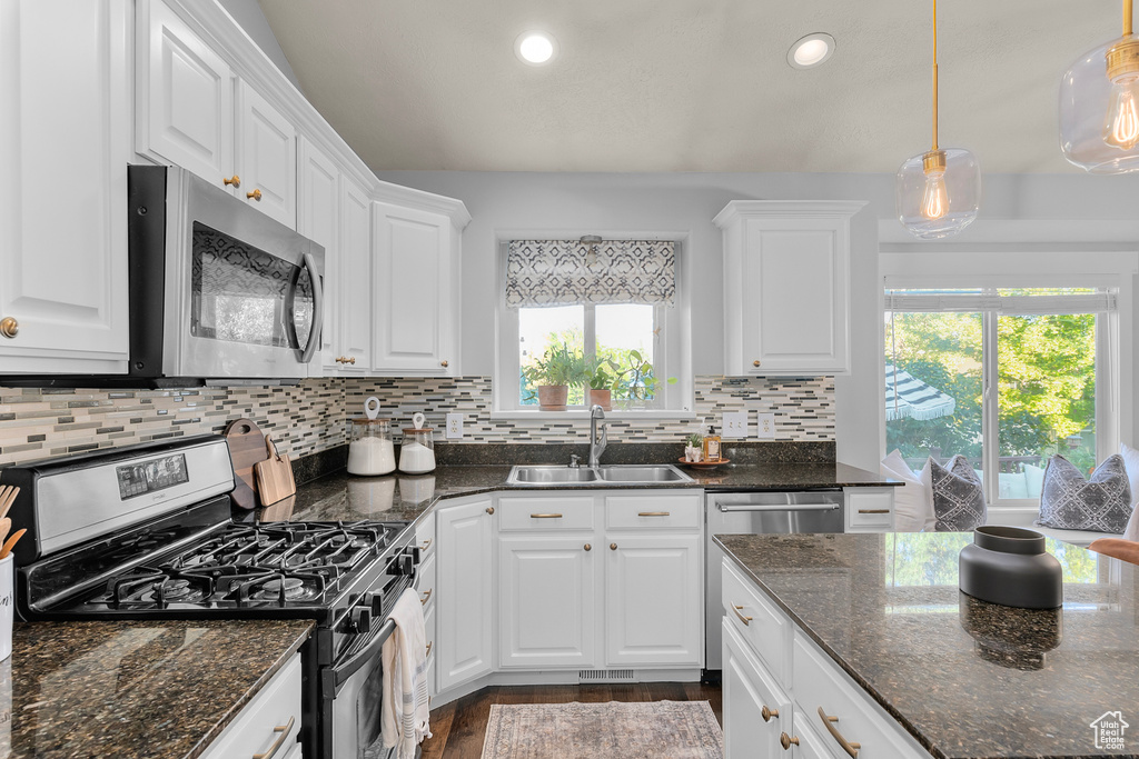 Kitchen featuring tasteful backsplash, white cabinets, sink, dark stone countertops, and stainless steel appliances