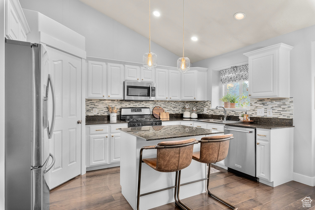 Kitchen with white cabinetry, appliances with stainless steel finishes, vaulted ceiling, and a kitchen island