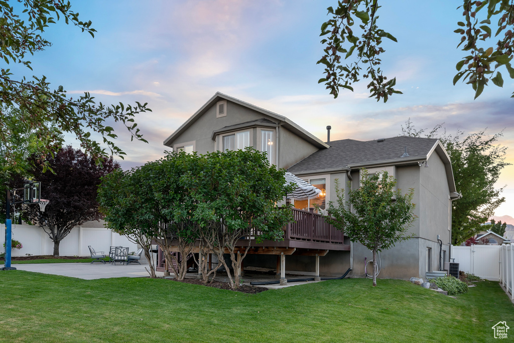 Back house at dusk featuring a patio area, cooling unit, a wooden deck, and a lawn