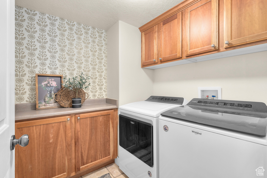 Laundry room with light tile patterned floors, washer and clothes dryer, a textured ceiling, and cabinets