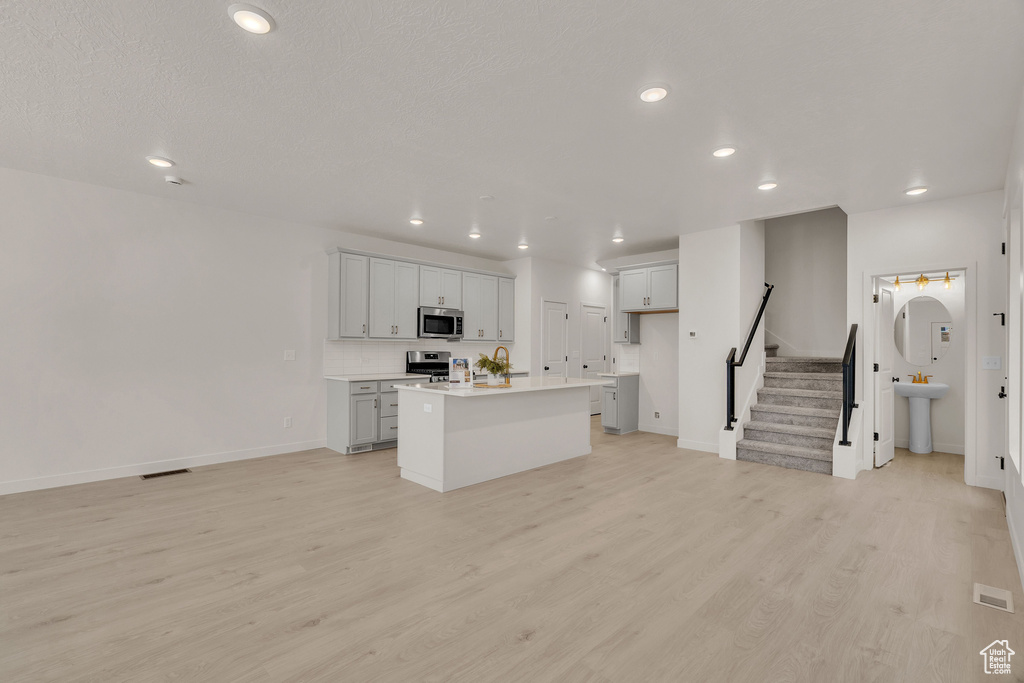 Kitchen with sink, a textured ceiling, a kitchen island with sink, stainless steel appliances, and light wood-type flooring