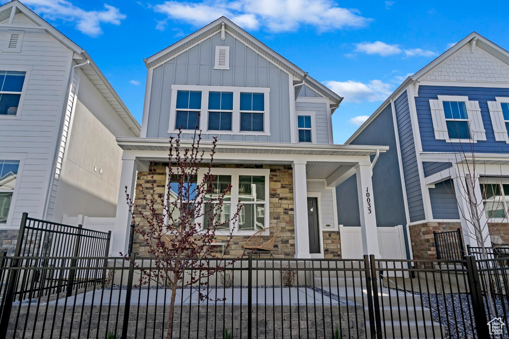View of front of property with a porch, stone siding, a fenced front yard, and board and batten siding
