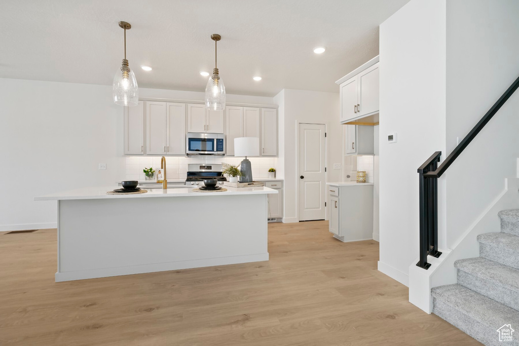 Kitchen featuring appliances with stainless steel finishes, decorative backsplash, light countertops, white cabinets, and light wood-type flooring