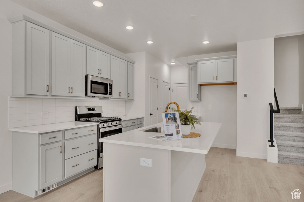 Kitchen with tasteful backsplash, stainless steel appliances, light hardwood / wood-style flooring, a kitchen island with sink, and sink