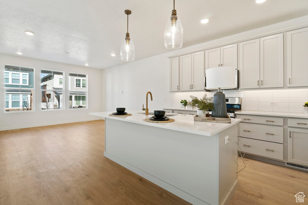 Kitchen with a sink, light countertops, a center island with sink, recessed lighting, and pendant lighting