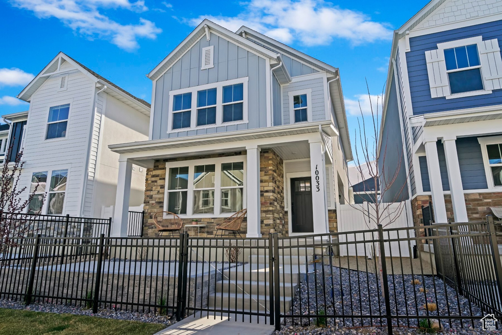 View of front of home featuring a porch, board and batten siding, stone siding, and a fenced front yard