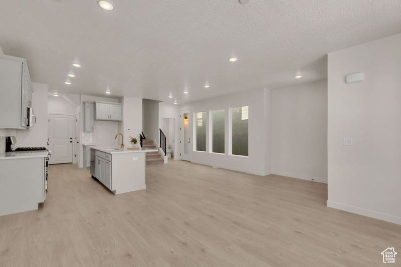 Kitchen featuring light hardwood / wood-style floors, an island with sink, white cabinets, a textured ceiling, and sink