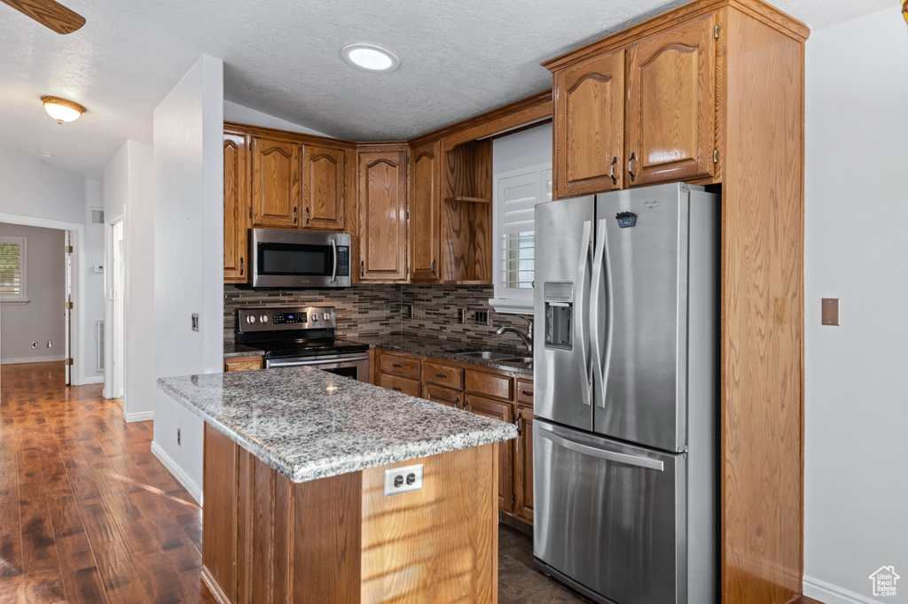 Kitchen featuring backsplash, sink, dark hardwood / wood-style flooring, stone countertops, and stainless steel appliances