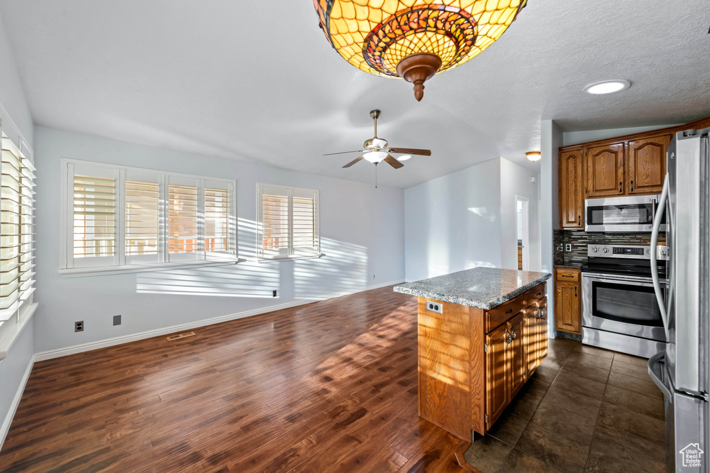 Kitchen with backsplash, a center island, dark tile patterned flooring, ceiling fan, and stainless steel appliances