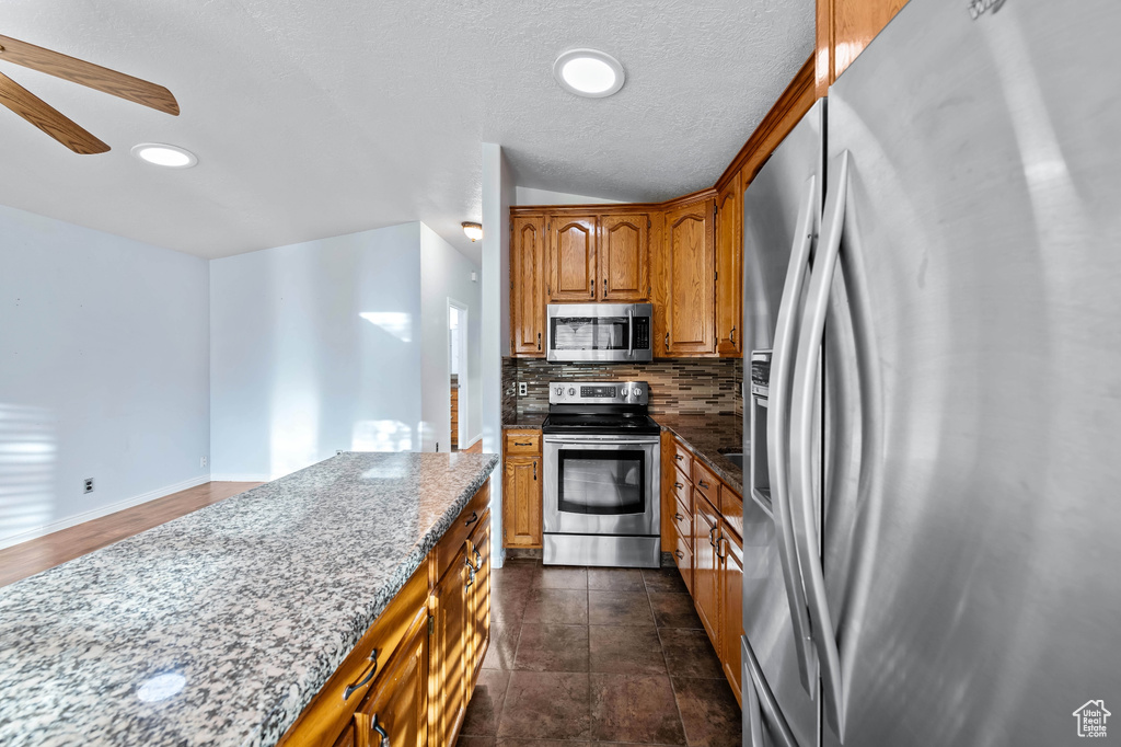 Kitchen featuring ceiling fan, decorative backsplash, light stone countertops, dark tile patterned floors, and stainless steel appliances