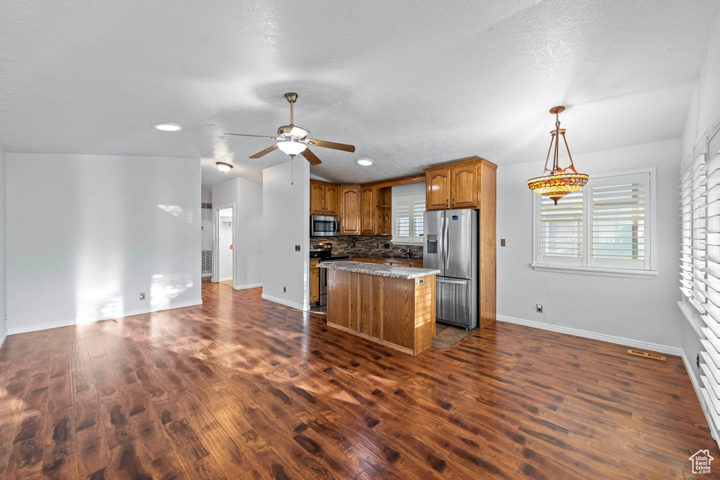 Kitchen with a center island, dark hardwood / wood-style flooring, decorative backsplash, ceiling fan, and stainless steel appliances