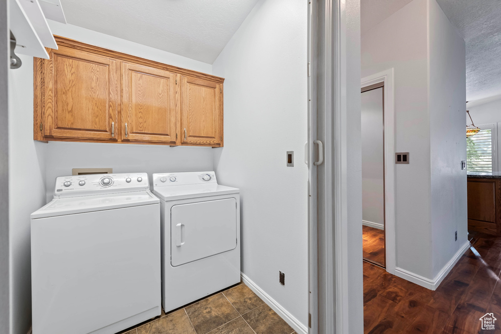 Clothes washing area with independent washer and dryer, dark hardwood / wood-style flooring, and cabinets