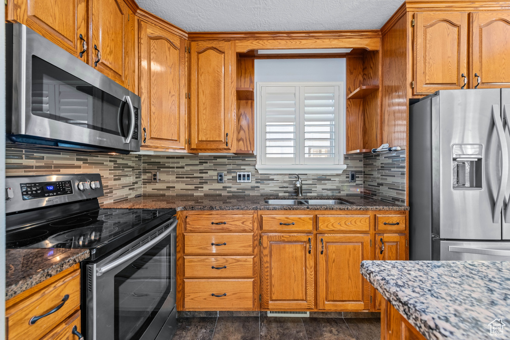 Kitchen with sink, dark stone countertops, appliances with stainless steel finishes, decorative backsplash, and dark tile patterned floors