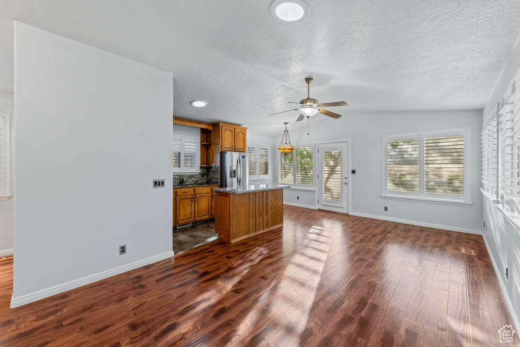 Unfurnished living room featuring ceiling fan, dark wood-type flooring, a textured ceiling, and lofted ceiling