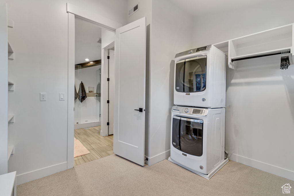 Laundry room with stacked washer and clothes dryer and light colored carpet