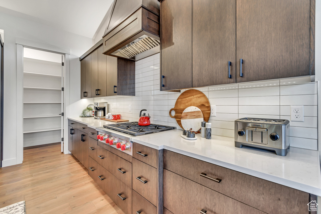 Kitchen with premium range hood, tasteful backsplash, stainless steel gas stovetop, light hardwood / wood-style floors, and lofted ceiling