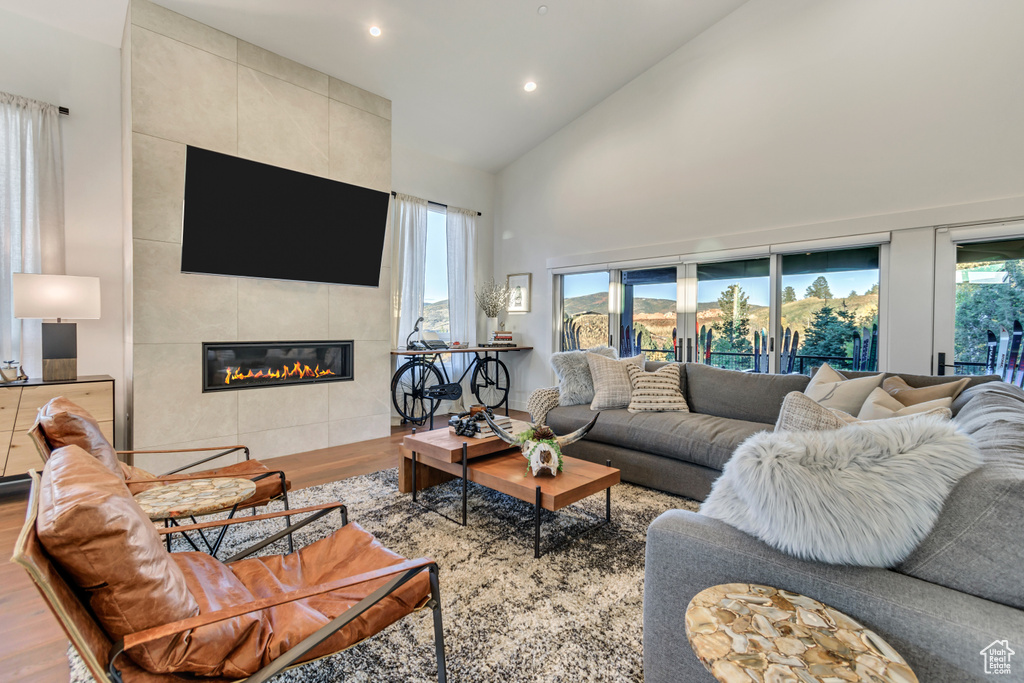 Living room featuring tile walls, a tiled fireplace, high vaulted ceiling, and wood-type flooring