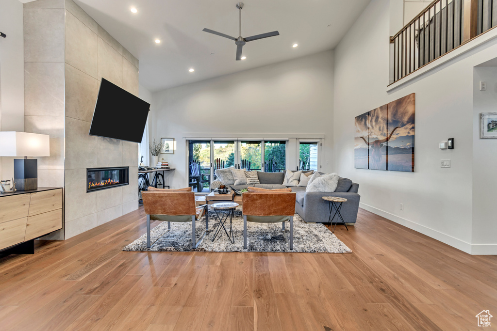 Living room featuring a fireplace, ceiling fan, light hardwood / wood-style floors, and high vaulted ceiling