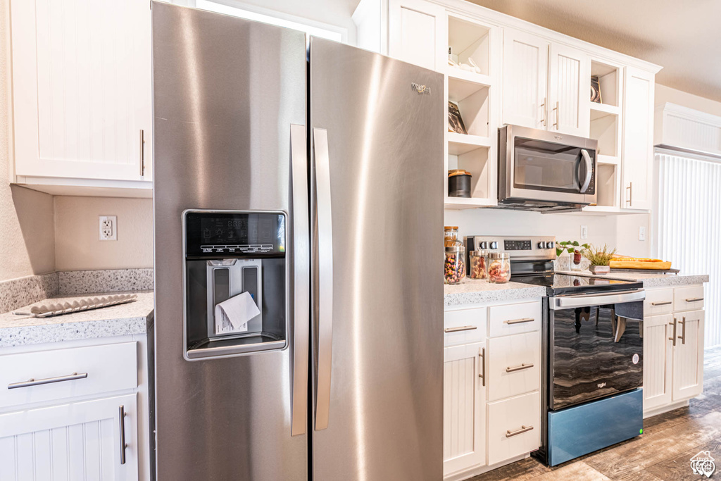 Kitchen with appliances with stainless steel finishes, light stone counters, white cabinetry, and light wood-type flooring