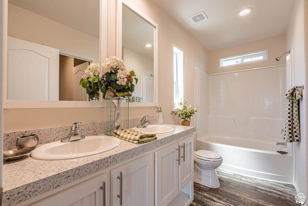 Full bathroom featuring double sink vanity, bathtub / shower combination, hardwood / wood-style floors, and toilet