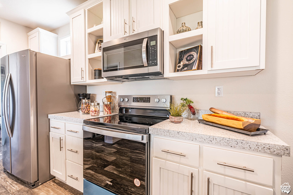 Kitchen featuring white cabinetry, light hardwood / wood-style floors, light stone counters, and stainless steel appliances