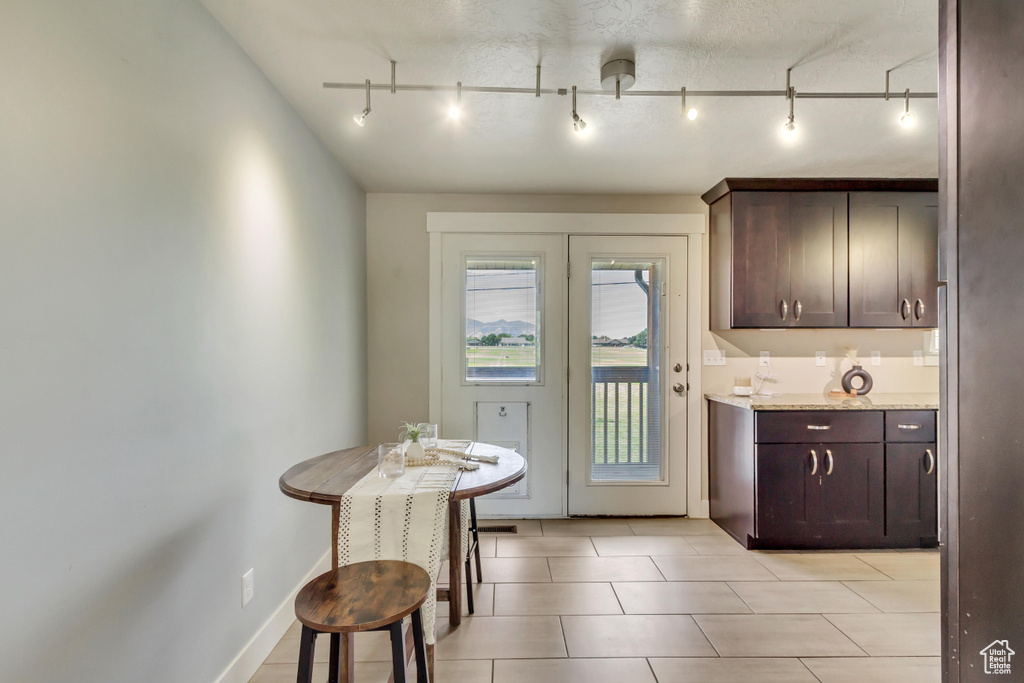 Kitchen with rail lighting, dark brown cabinetry, light stone countertops, a textured ceiling, and light tile patterned floors