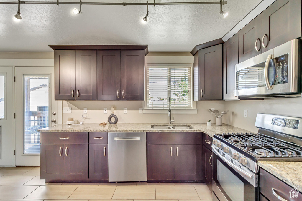 Kitchen with sink, appliances with stainless steel finishes, rail lighting, light stone countertops, and a textured ceiling