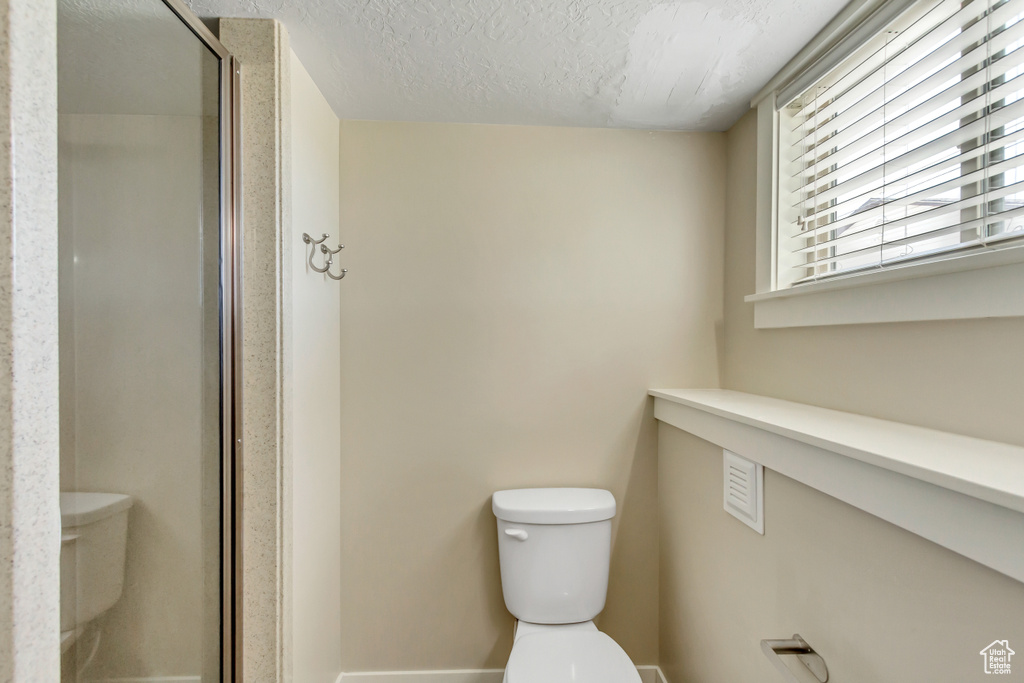 Bathroom with a textured ceiling, an enclosed shower, and toilet