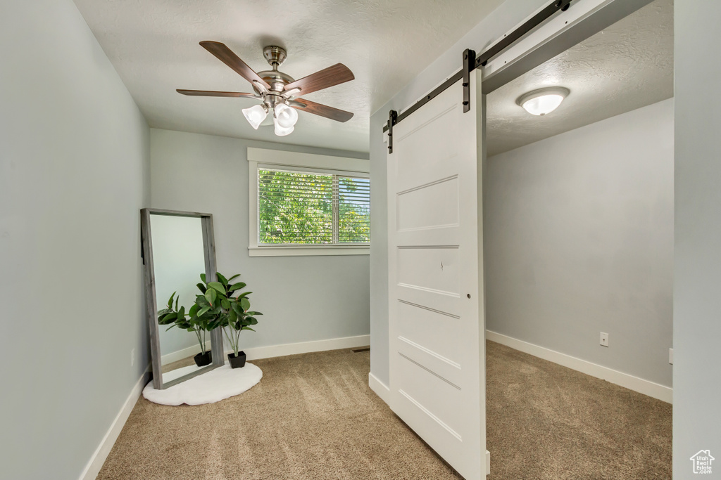 Unfurnished bedroom with ceiling fan, light carpet, and a barn door