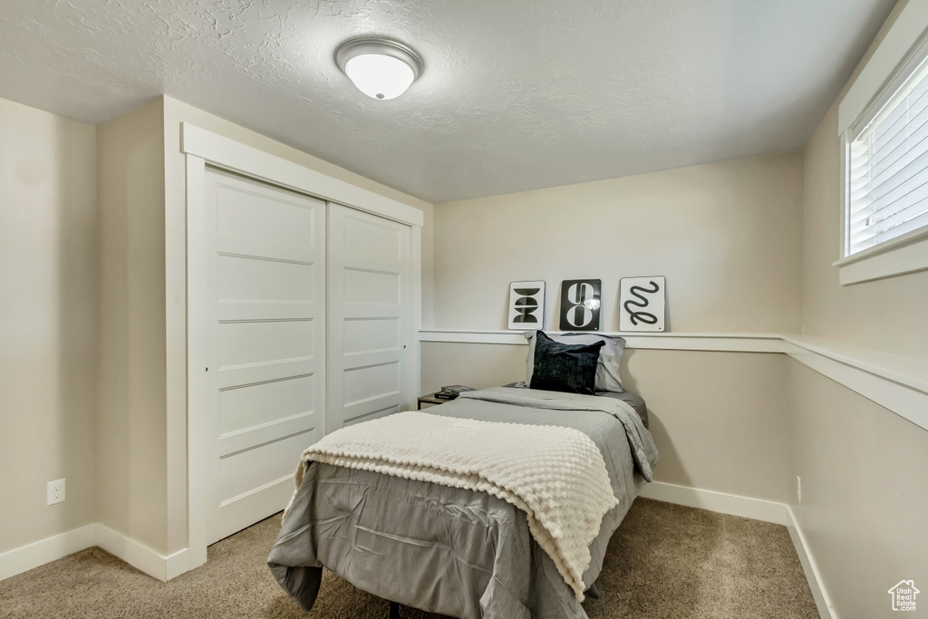 Bedroom with a closet, light colored carpet, and a textured ceiling