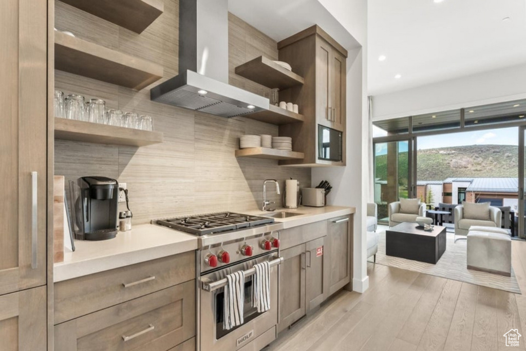 Kitchen featuring sink, luxury range, light hardwood / wood-style flooring, tasteful backsplash, and wall chimney range hood