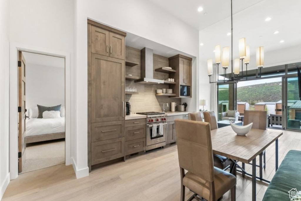 Kitchen featuring backsplash, light hardwood / wood-style floors, hanging light fixtures, wall chimney range hood, and luxury stove