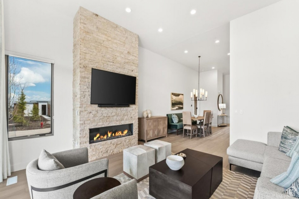 Living room featuring light wood-type flooring, a towering ceiling, a notable chandelier, and a fireplace