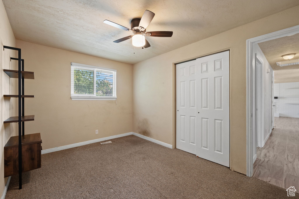 Unfurnished bedroom featuring a closet, a textured ceiling, light carpet, and ceiling fan