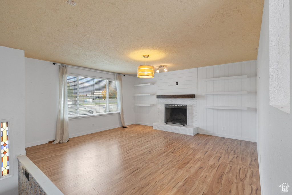 Unfurnished living room featuring a brick fireplace, a textured ceiling, and light hardwood / wood-style flooring