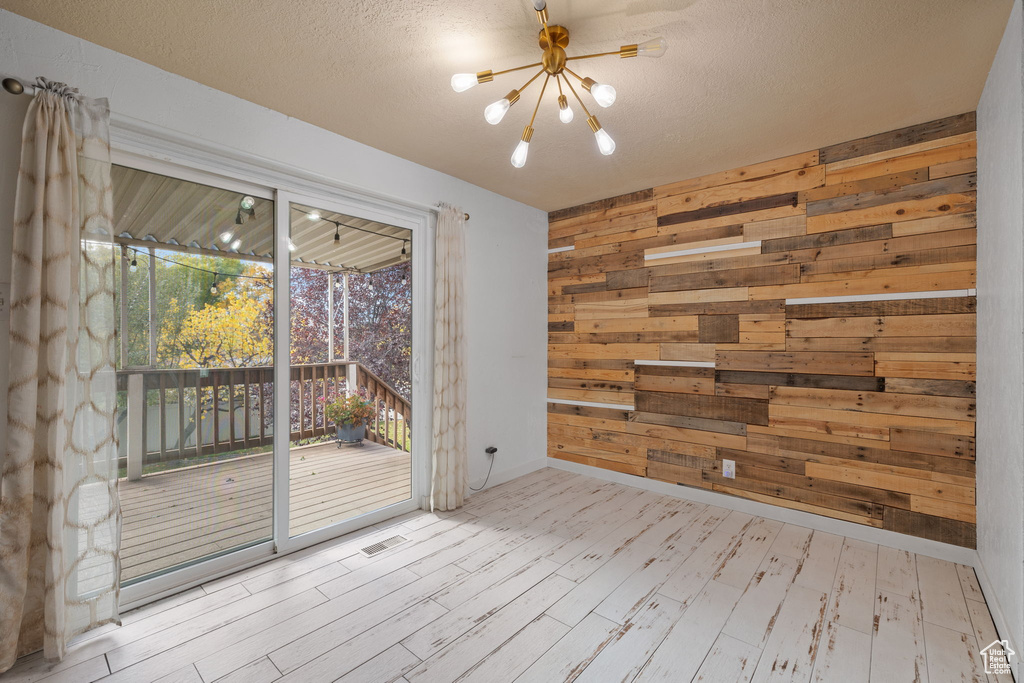 Empty room with light hardwood / wood-style floors, wooden walls, and a textured ceiling