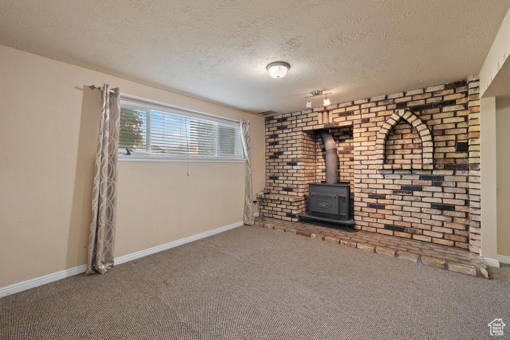 Unfurnished living room with a textured ceiling, a wood stove, and carpet floors