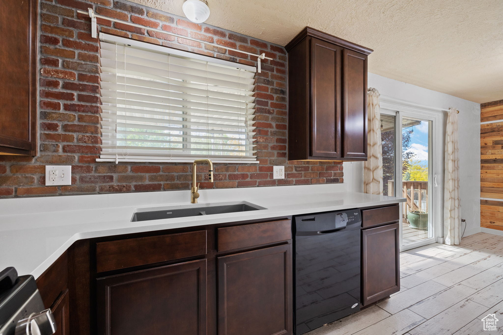 Kitchen featuring black dishwasher, dark brown cabinetry, wood walls, sink, and light wood-type flooring