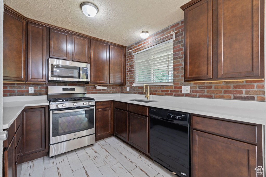 Kitchen featuring sink, a textured ceiling, dark brown cabinetry, and stainless steel appliances