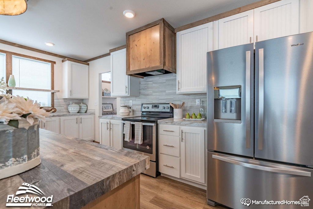 Kitchen with light hardwood / wood-style floors, stainless steel appliances, tasteful backsplash, and white cabinets