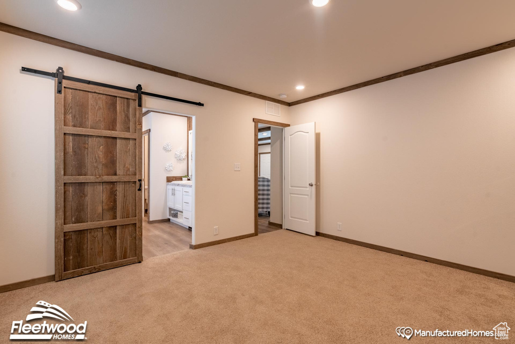 Unfurnished bedroom with a barn door, connected bathroom, light carpet, and crown molding