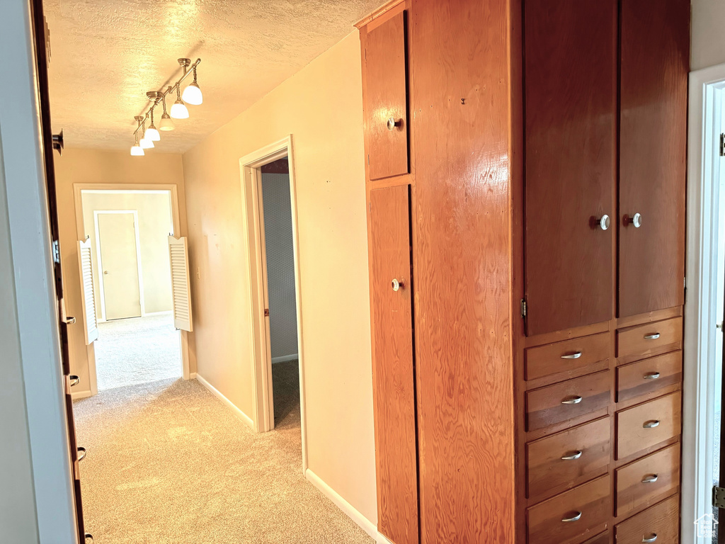 Hallway featuring light carpet, track lighting, and a textured ceiling