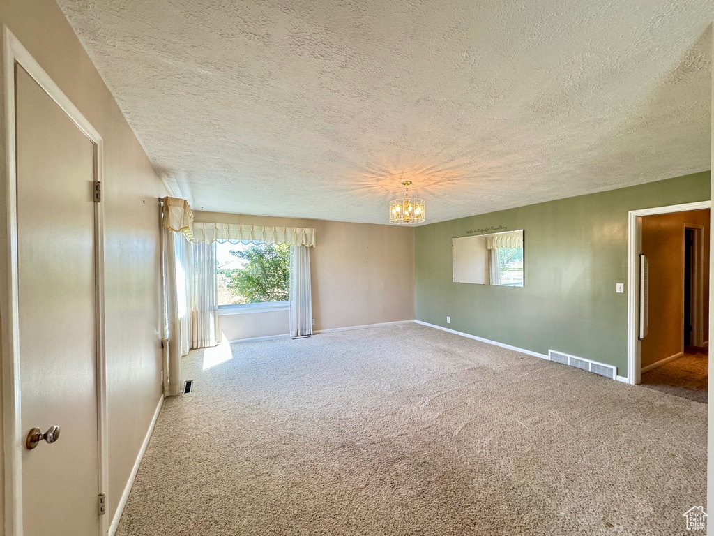 Empty room with carpet, a notable chandelier, and a textured ceiling