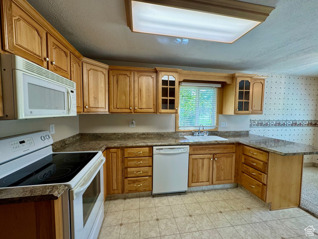 Kitchen with sink, a textured ceiling, light tile patterned floors, kitchen peninsula, and white appliances