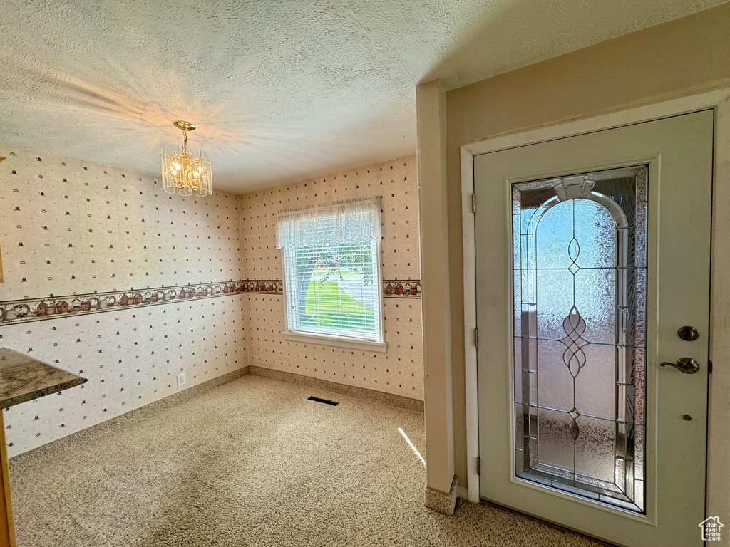 Carpeted entryway featuring a textured ceiling and a chandelier